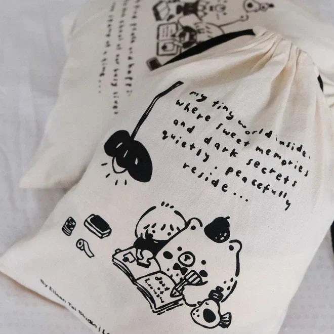 Cloth drawstring pouch with cute black illustrations and handwritten-style text, featuring a cozy character drawing and minimal doodles on a soft white fabric.