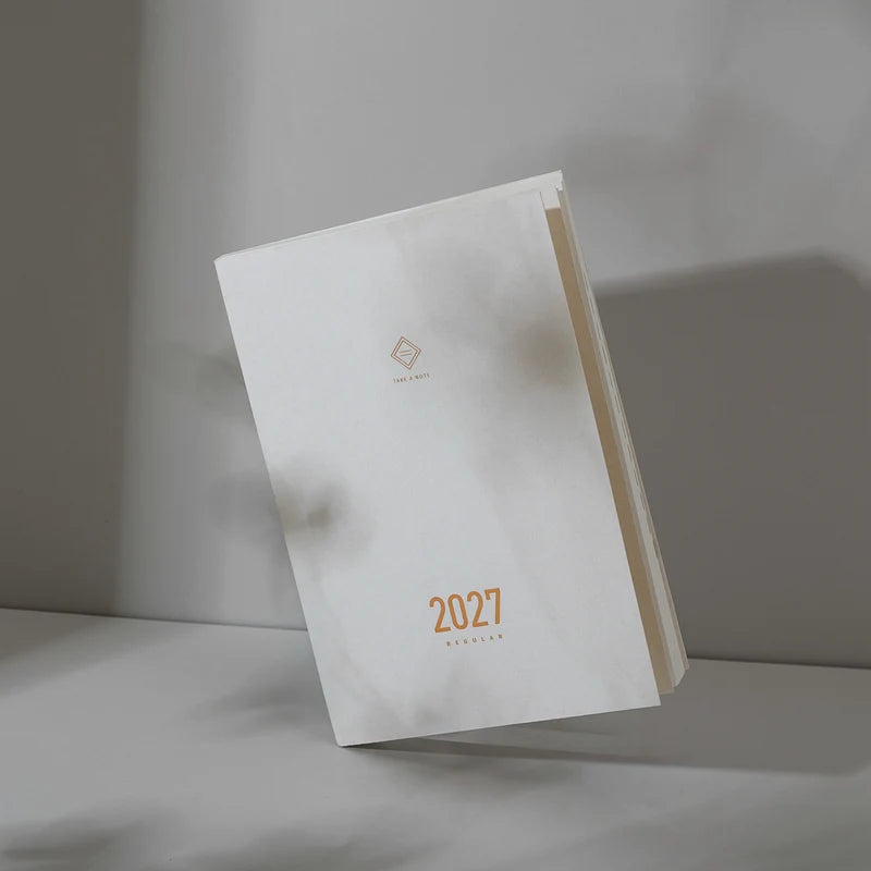 2027 Regular Planner A5 by Take a Note — white planner standing upright with gold-foil cover detail, for planning
