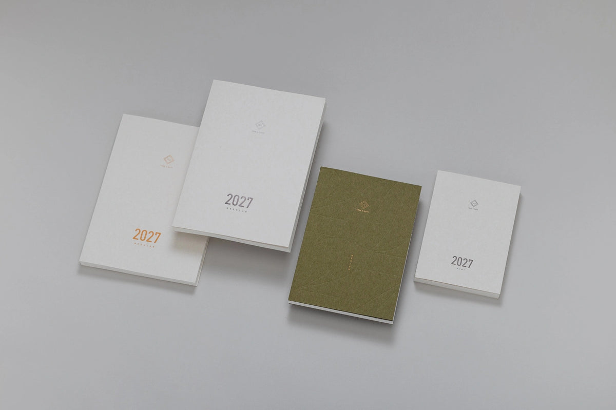 Four minimalist Take a note planner 2027 publication covers or boxes arranged on a light gray background, including two white pieces with gold '2027' text, one white piece with a small gold emblem, and one textured olive-green piece.