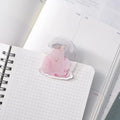 Red Ribbon Journaling Clip by Dodolulu — translucent pink figure acrylic clip on a grid notebook, for journaling