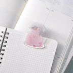 Red Ribbon Journaling Clip by Dodolulu — translucent pink figure acrylic clip on a grid notebook, for journaling