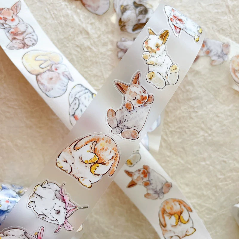 Roll of Cute Rabbit Ji A34 PET Tape with animal illustrations resting on a textured surface
