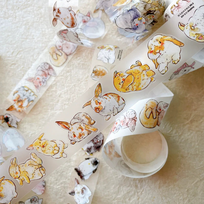 Rolls of Cute Rabbit Ji A34 PET Tape with cute animal designs on a textured surface, top view