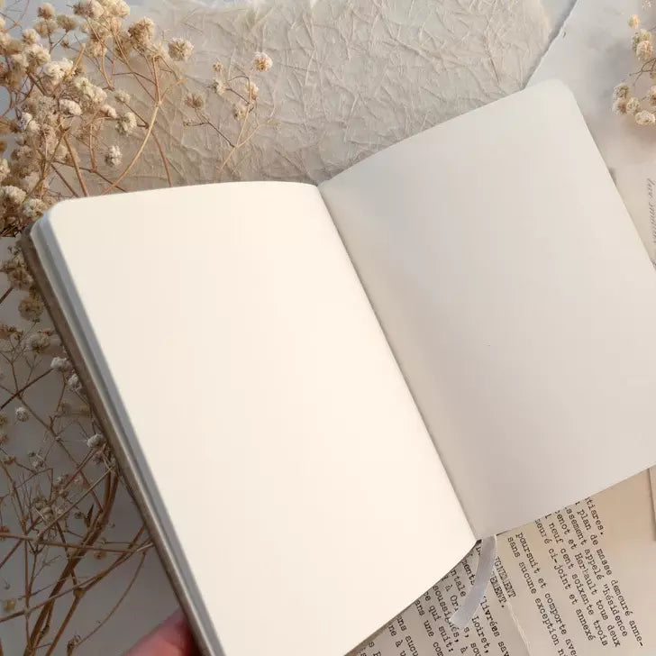 Open A6 Blank Notebook with a softly blurred floral background on a textured surface