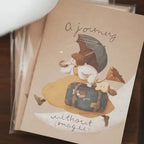 Card with a cartoon character in a hat and suitcase, surrounded by stars, on a wooden surface.