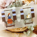 Decorative stickers with illustrations of a person and a cat on a balcony, placed on a textured surface with flowers.