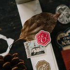 Close-up of a box with a red and white logo, a leaf, and a pine cone on a dark background.