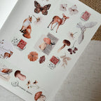 Sheet of nature-themed stickers with animals, plants, and stamps on a textured surface.