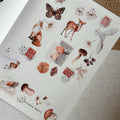 Sheet of decorative stickers with animals, flowers, and stamps on a textured surface.