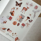 Sheet of decorative stickers with animals, flowers, and stamps on a textured surface.
