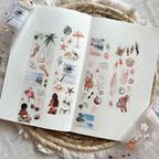 Open book with beach-themed stickers on a woven surface