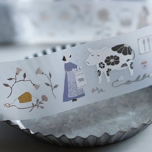 Strip of At The Farm PET Tape with a cow, figure and cake designs on a textured surface