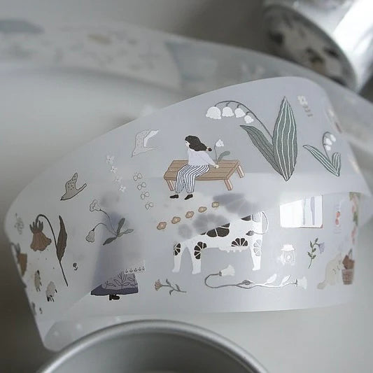 Decorative teapot lid with illustrations of a woman, cow, and plants.