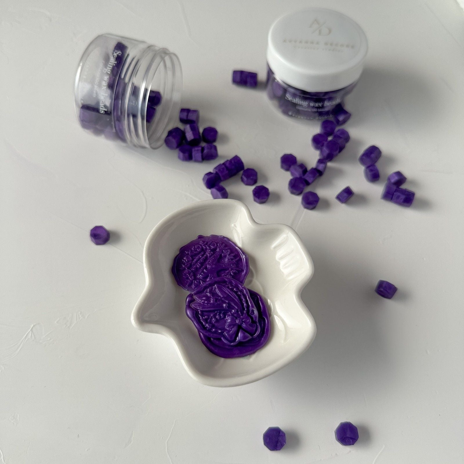 Purple decorative items in a white dish with two containers on a light gray background
