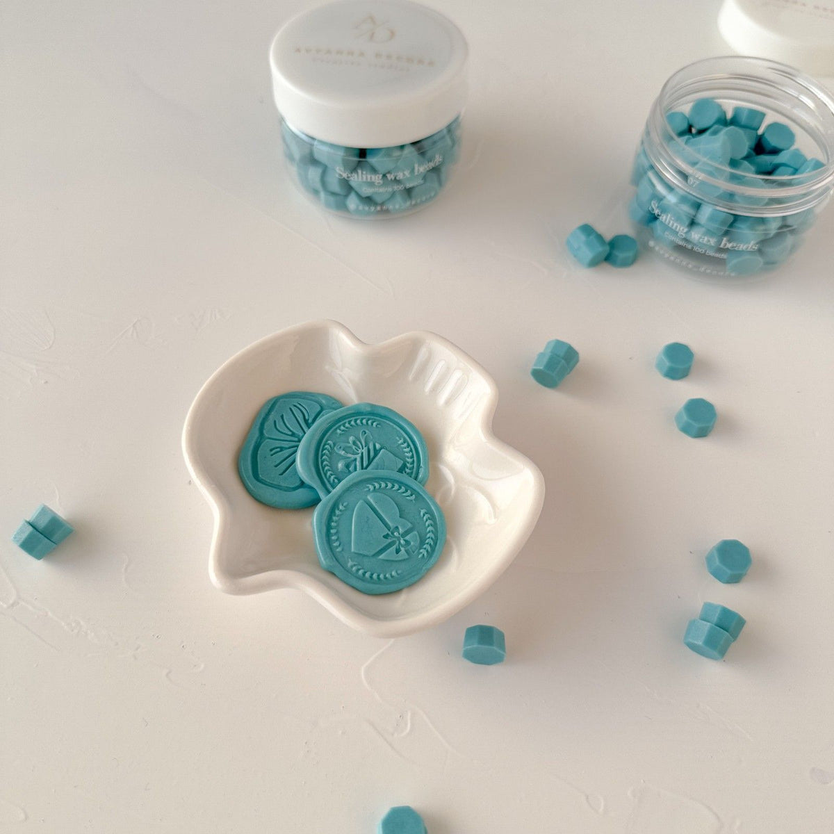 Pastel Baby Blue Wax Beads pieces in a white dish with storage jars behind, styled on a light surface