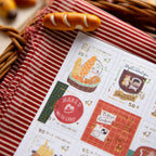 Sheet of decorative stamps with bakery-themed designs on a red and white striped fabric background.