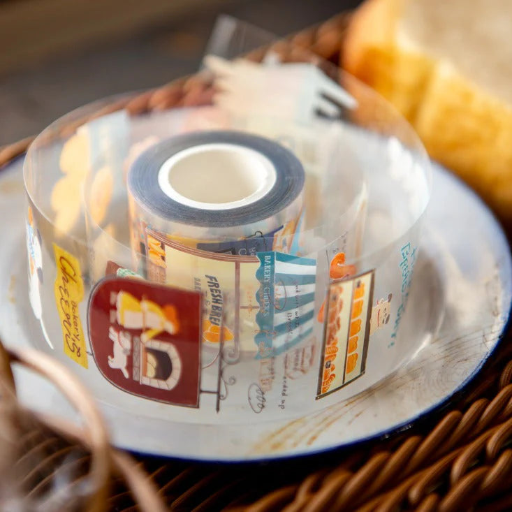 Roll of Bakery Cheer's PET Tape with printed bakery labels resting on a woven surface