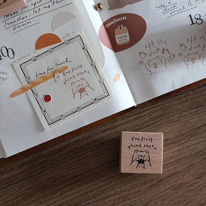 Wooden stamp with 'Eat first, think later' text on a wooden surface with a book in the background.