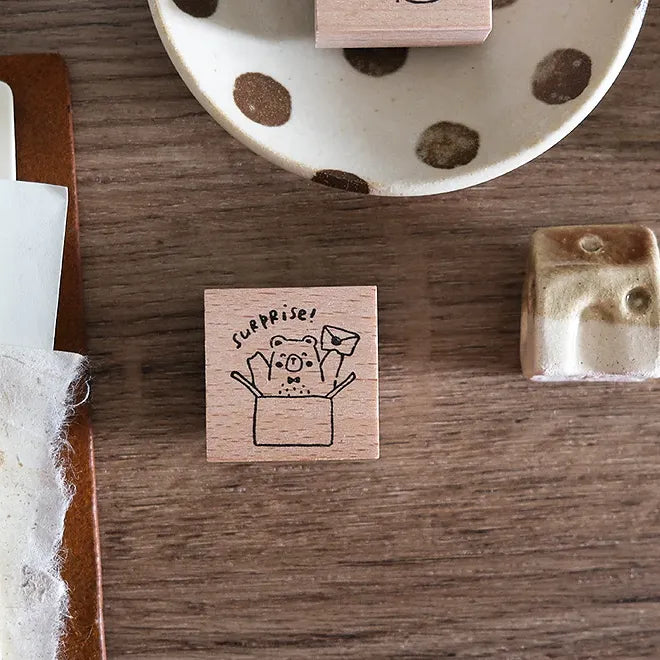 Wooden stamp with 'surprise!' design on a wooden surface