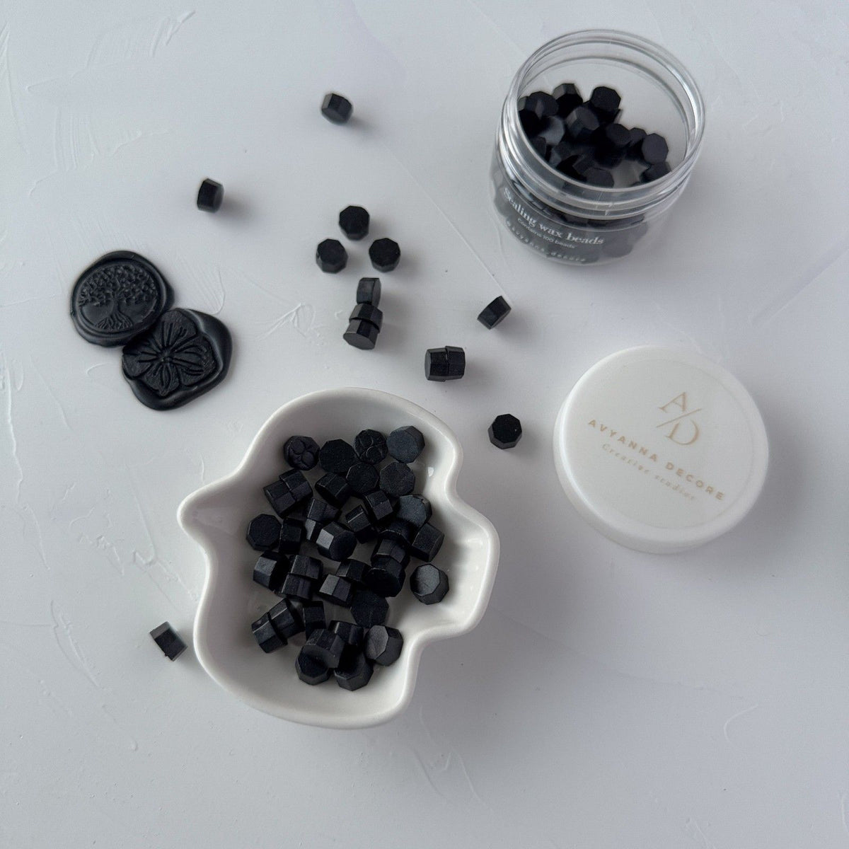 Jet-black stamped wax seal made from Black Wax Beads displayed on a white branded surface, close-up view