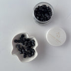 Black hexagonal beads in a small dish and jar on a white surface with 'A+D' branding.