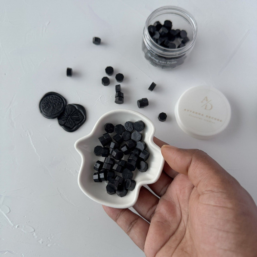 Hand holding a white dish filled with black hexagonal tablets, with a jar and lid in the background on a light gray surface.
