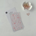 Floral sticker sheet with a white dish containing paper clips on a light gray background