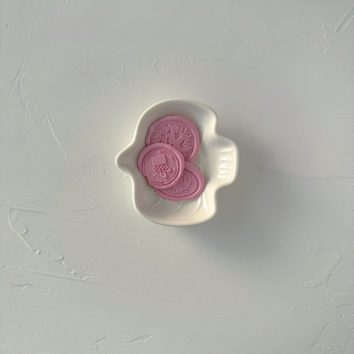 Two soft pink Blossom Wax Beads seals in a shaped white dish on a light grey background