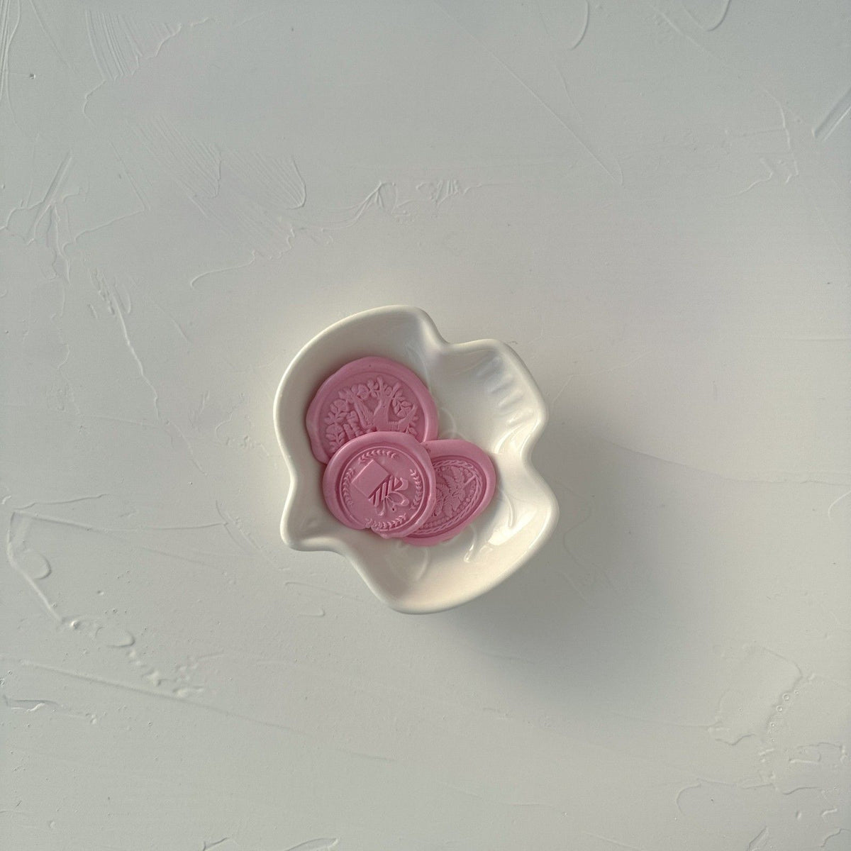 Three soft pink Blossom sealing wax seals in a white heart-shaped dish on light grey