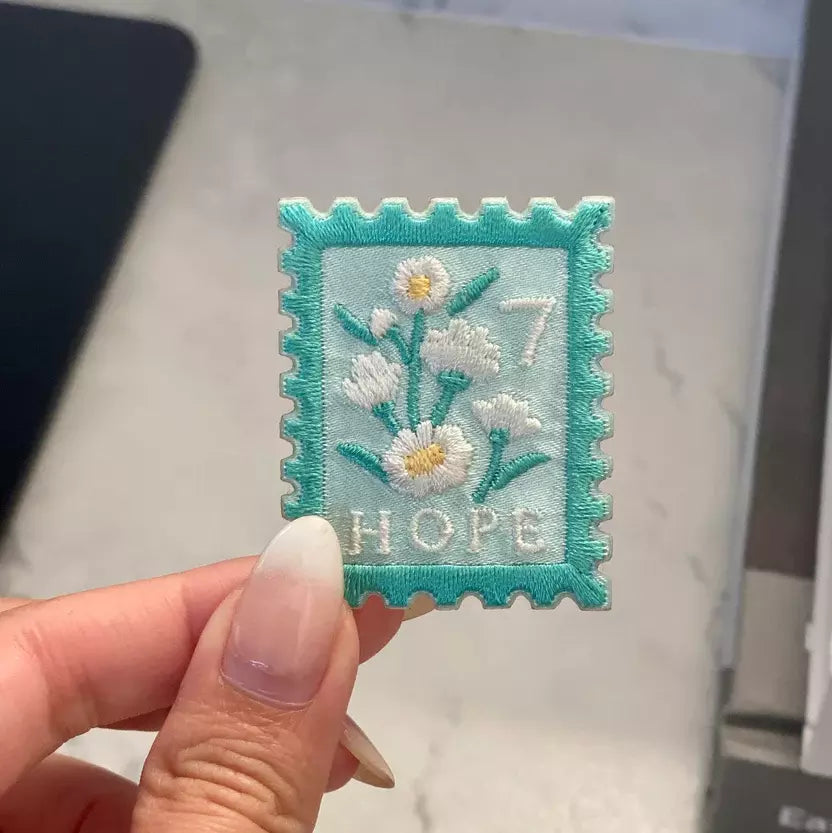 Embroidered patch with flowers and 'Hope' text held by a hand