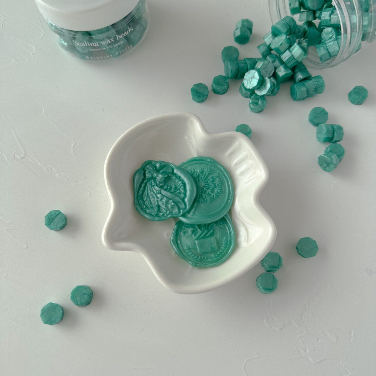 Blue Lagoon Wax Beads filling a white dish beside the open storage jar of loose beads on a light background