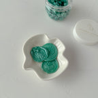 Green wax melts in a white dish on a light gray background