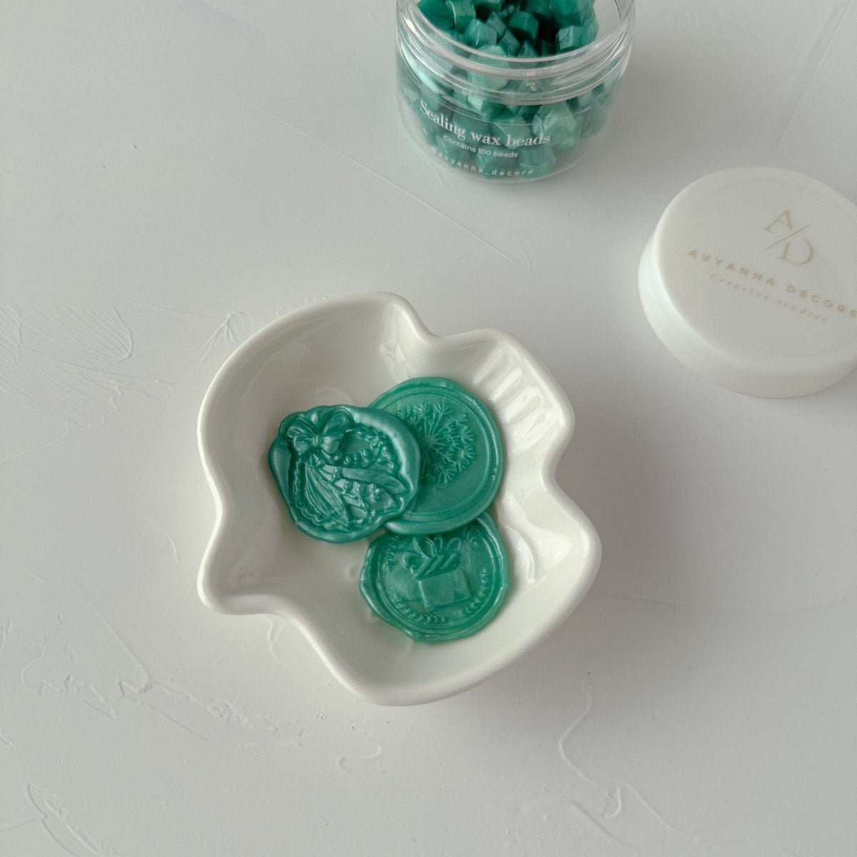 Melted Blue Lagoon sealing wax discs displayed in a small white dish, top view on a light grey background