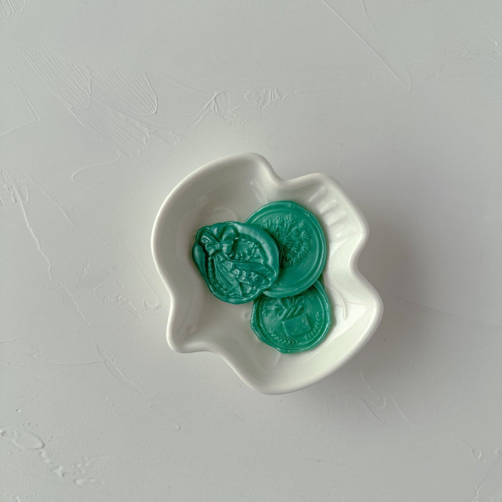 Three green coins in a white wavy dish on a light gray background