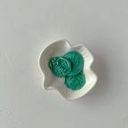 Three green coins in a white wavy dish on a light gray background