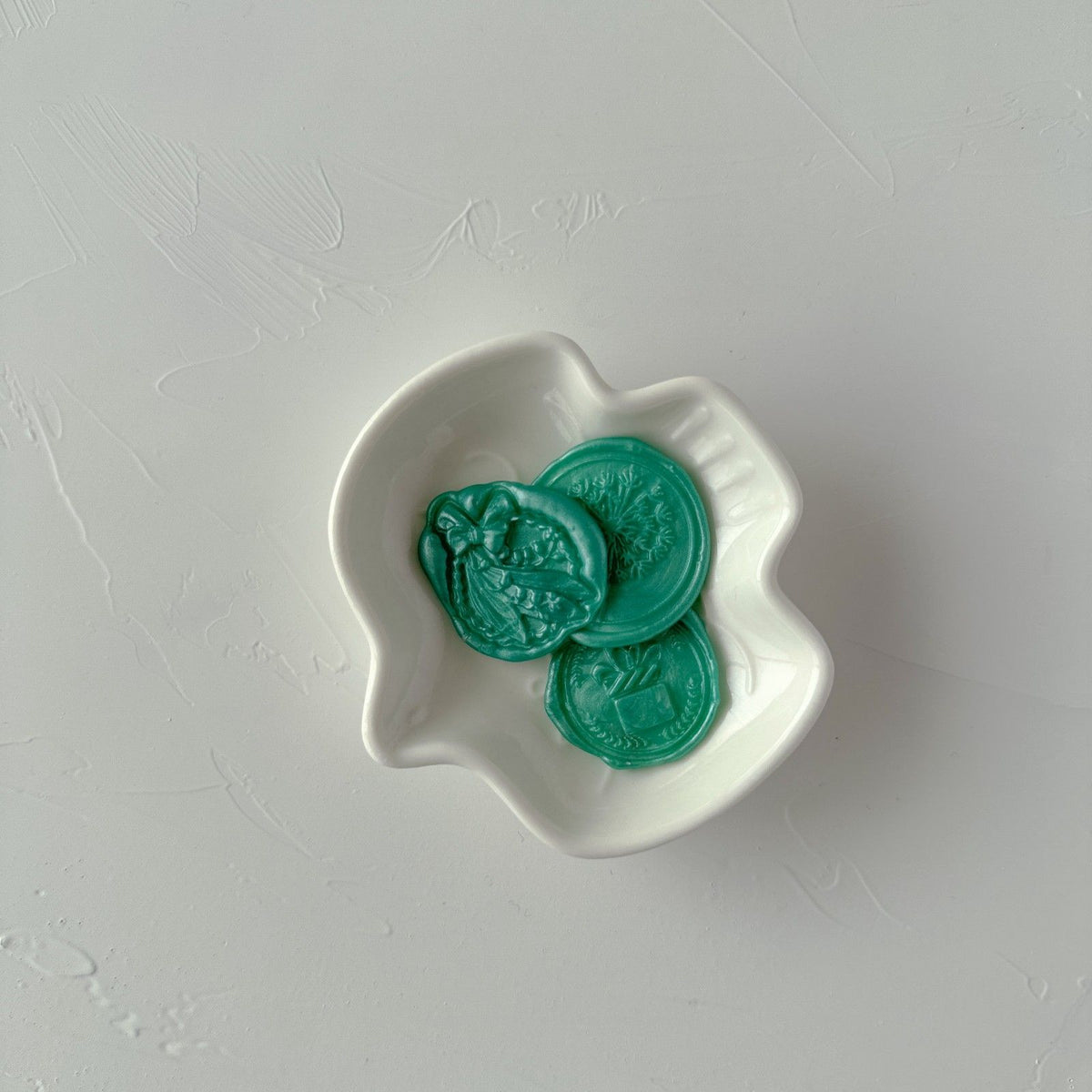 Three round Blue Lagoon wax bead discs displayed in a wavy-edged white dish on a light grey backdrop