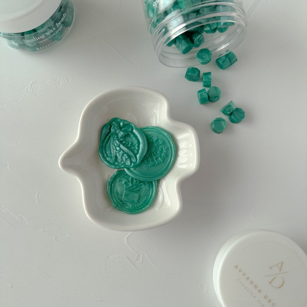 Stamped wax seals made from Blue Lagoon Wax Beads in a white dish with an open jar of beads behind them