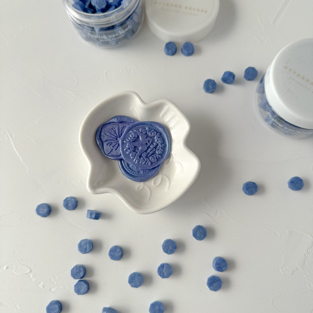Heart-shaped Blue Pottery sealing wax pieces in a white dish with beads scattered on a grey backdrop