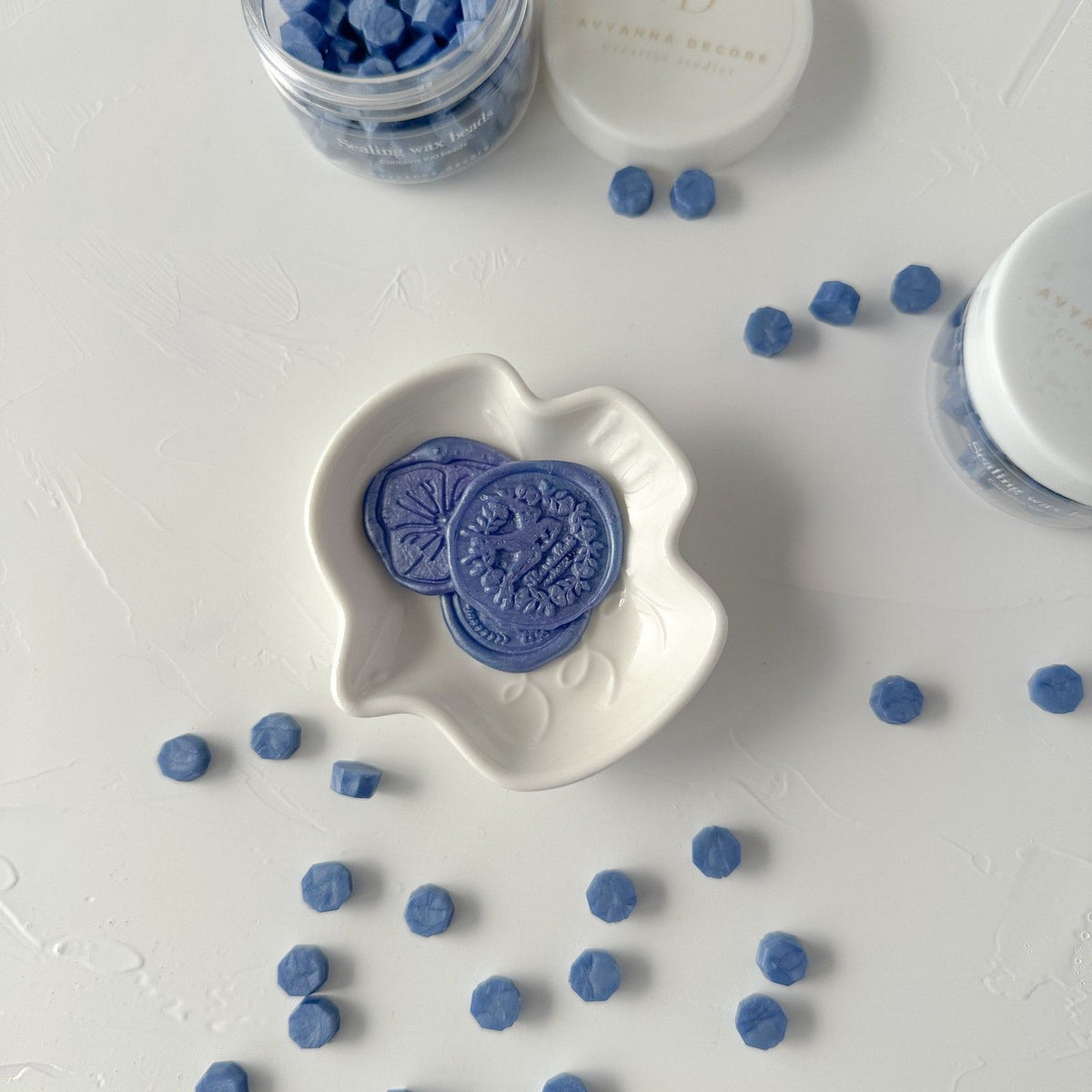 Round Blue Pottery Wax Beads with one crumbled bead showing wax texture, close-up on a white surface