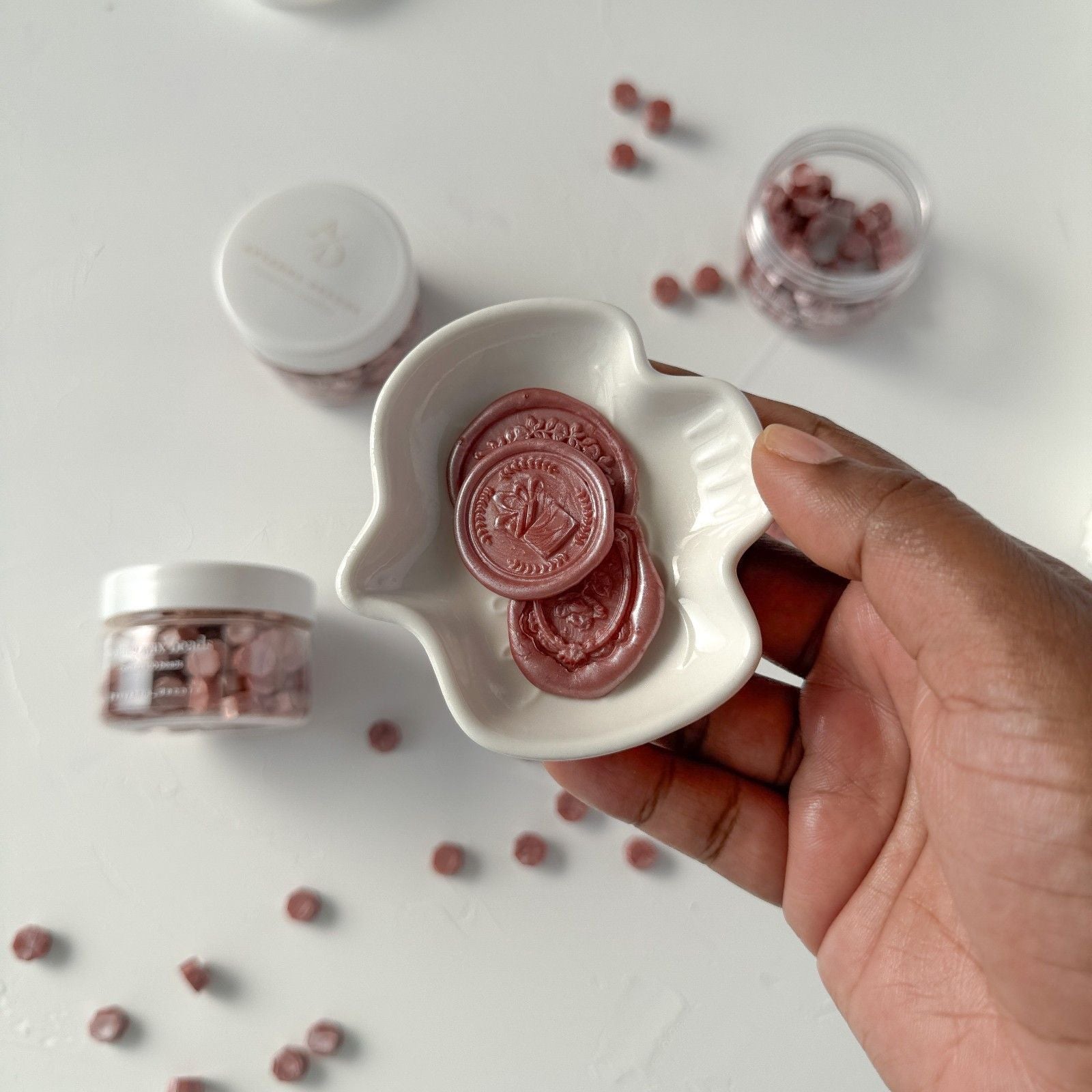 Hand holding a white dish with pink circular objects on a light background
