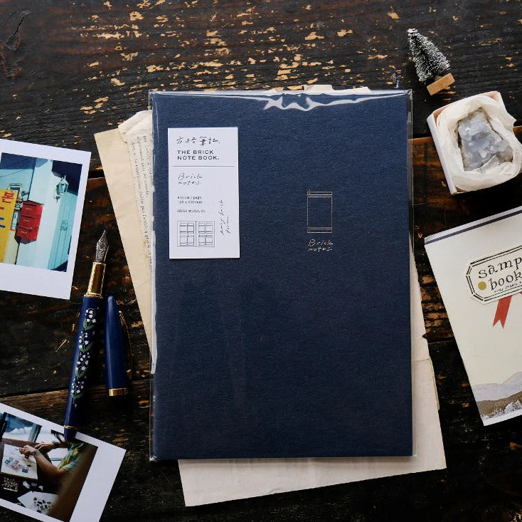 Brick Notes Notebook by OURS Studio in blue with a pen and photos on a wooden surface