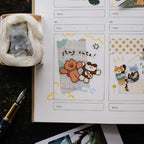 Notebook with cute illustrations of animals and text, next to a fountain pen on a wooden surface.