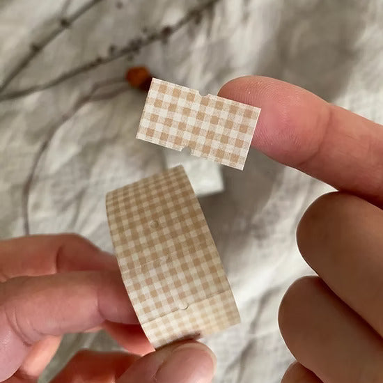 Two Brown Plaid Label Sticker Tape checkered labels by Hairmo held between fingers, close-up