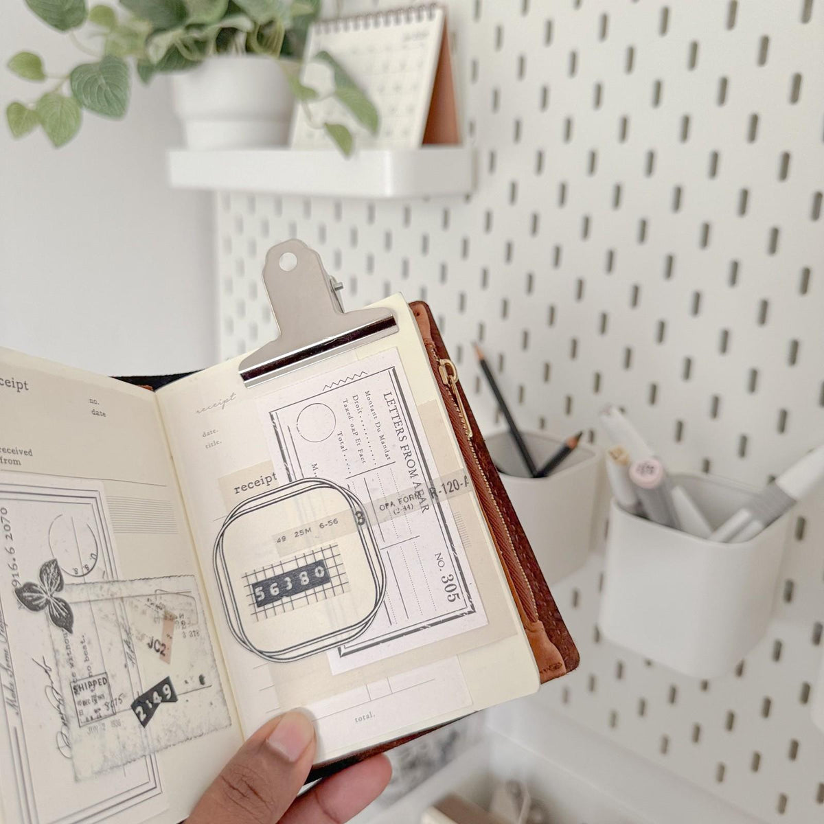 Illustrated notebook held open with the Large 2 inch Bulldog Clip beside a plant on white