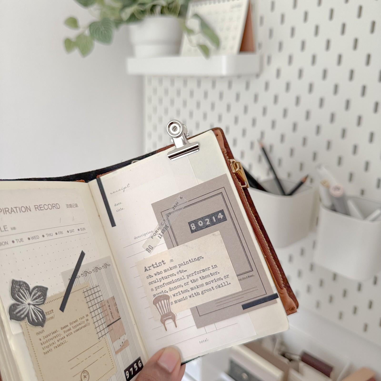 Open notebook with illustrations held by a hand, blurred indoor background