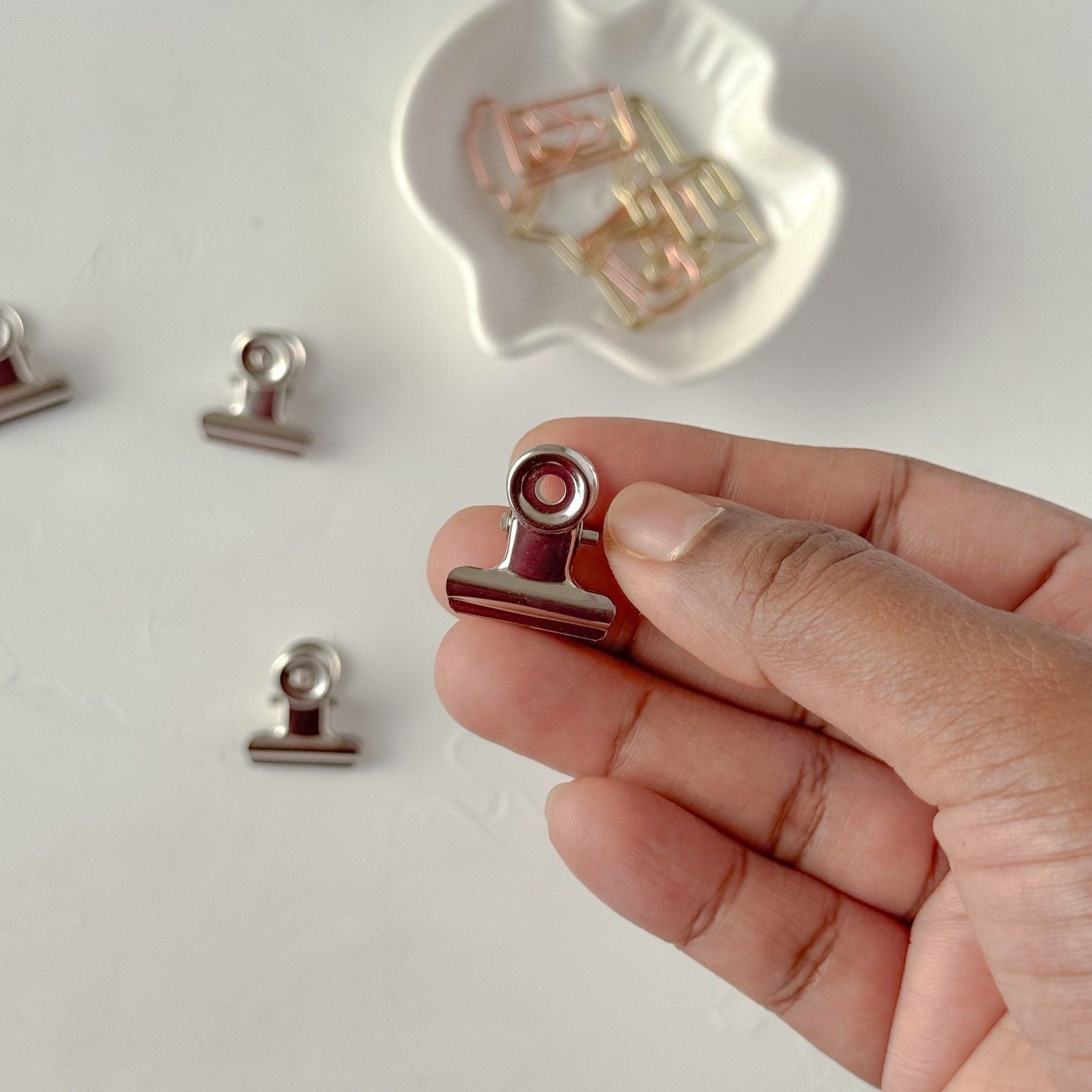 Hand holding a small metal clip with a blurred background