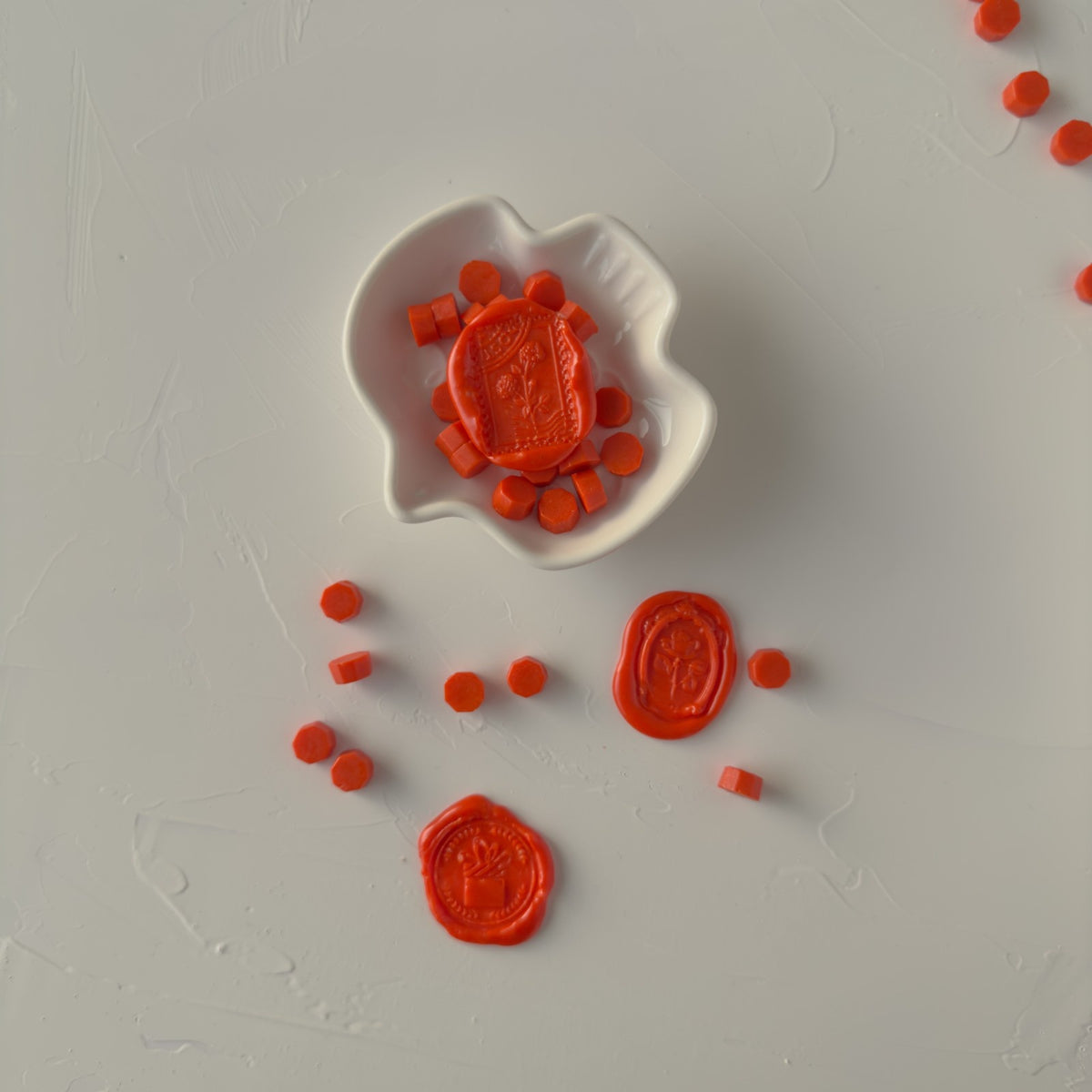 Burnt Orange Wax Beads with stamped wax seals and a small white dish arranged on a light grey backdrop