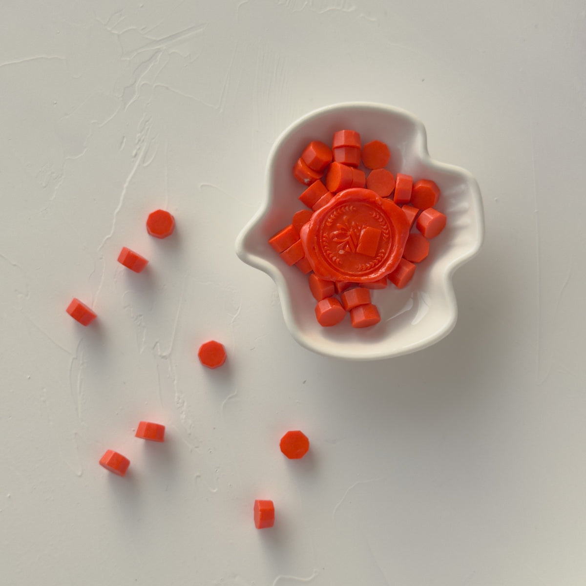 Rich burnt orange sealing wax bead pieces with a seal mold at the centre, flat lay on a white background
