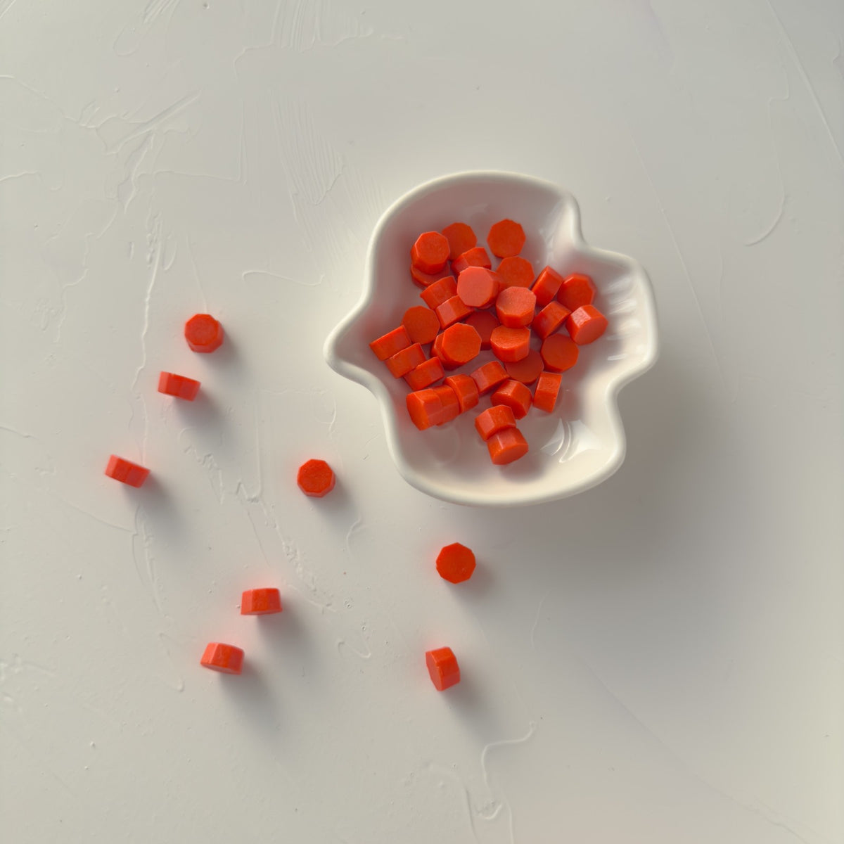 Leaf-shaped white dish holding Burnt Orange Wax Beads pieces styled on a soft light grey background