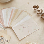 Collection of handmade paper samples on a textured surface with a dried plant.